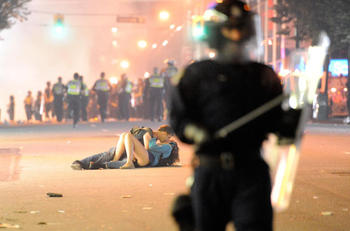 VANCOUVER, BC - JUNE 15:  Riot police walk in the street as a couple kiss on June 15, 2011 in Vancouver, Canada. Vancouver broke out in riots after their hockey team the Vancouver Canucks lost in Game Seven of the Stanley Cup Finals.  (Photo by Rich Lam/G
