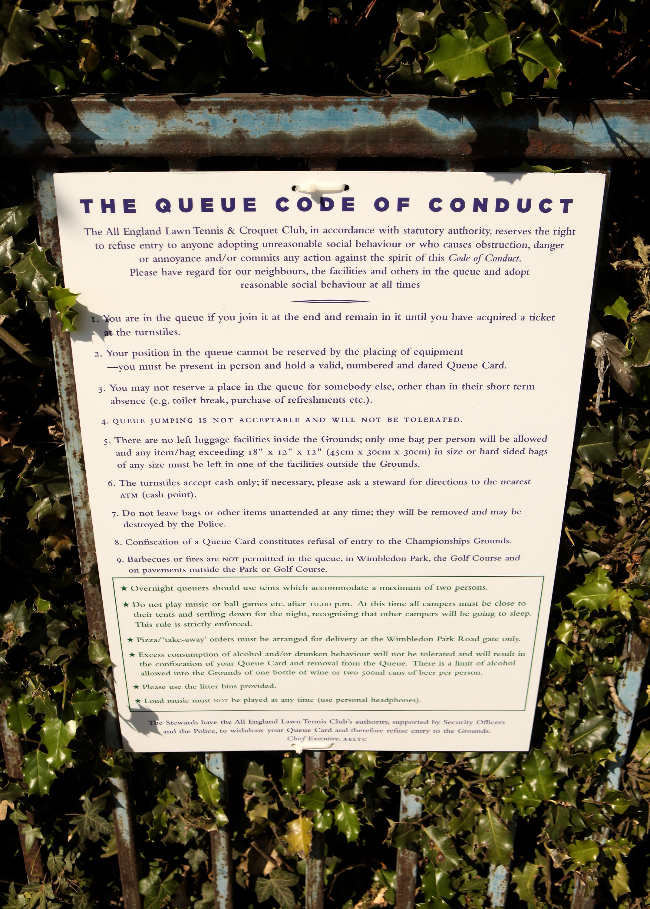 LONDON, ENGLAND - JUNE 21:  A 'queue code of conduct' notice is attached to a railing adjacent to members of the public queuing for tickets on the opening day of the Wimbledon tennis championships on June 21, 2010 in London, England. The prestigious grass